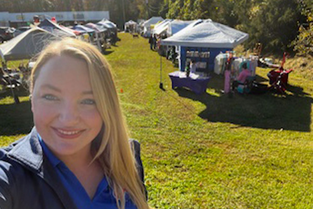 female on bright sunny day smiling and taking selfie at Summerfield Farms event